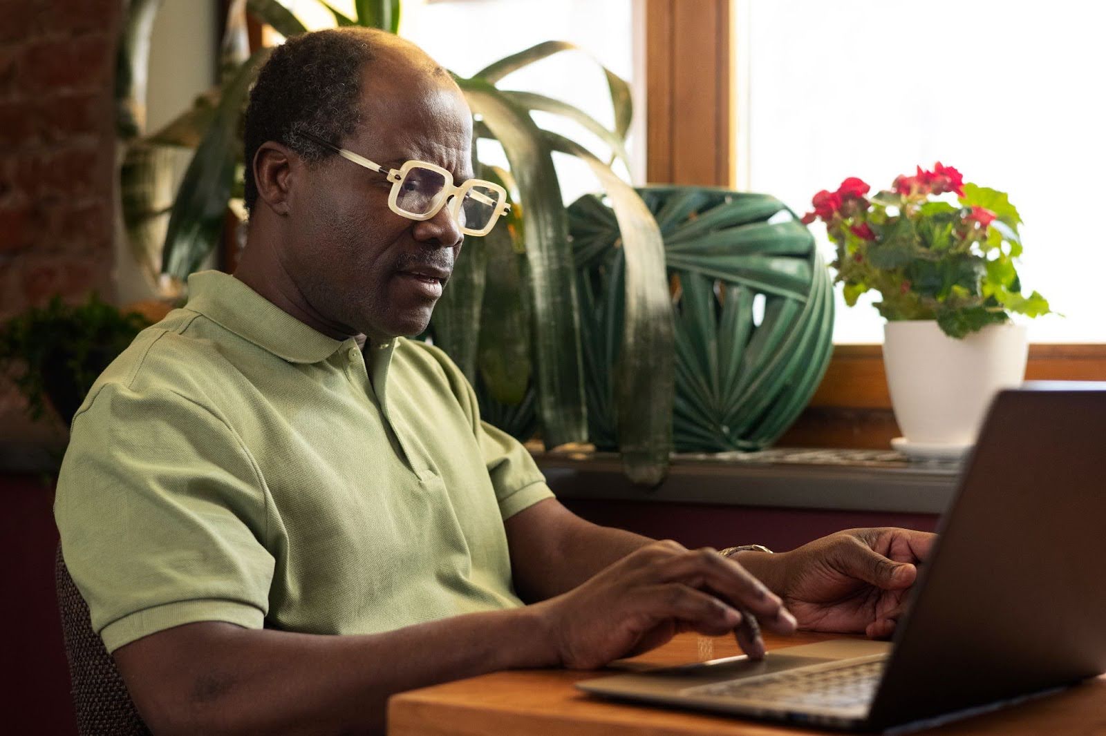 Um homem afro-brasileiro de camisa verde e óculos tecla em um notebook pesquisando sobre os tipos de aposentadoria.