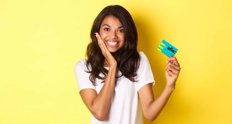 Uma mulher sorridente, com cabelo solto, segura um cartão de crédito. A imagem ilustra um sentimento positivo sobre como cancelar compra no cartão de crédito.