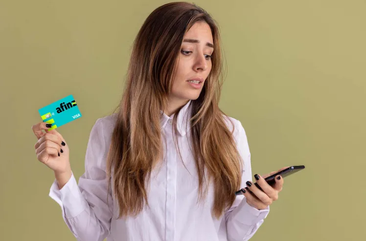 Mulher com expressão preocupada, usando uma camisa branca e segurando um cartão, refletindo a incerteza em como cancelar compra no cartão de crédito.