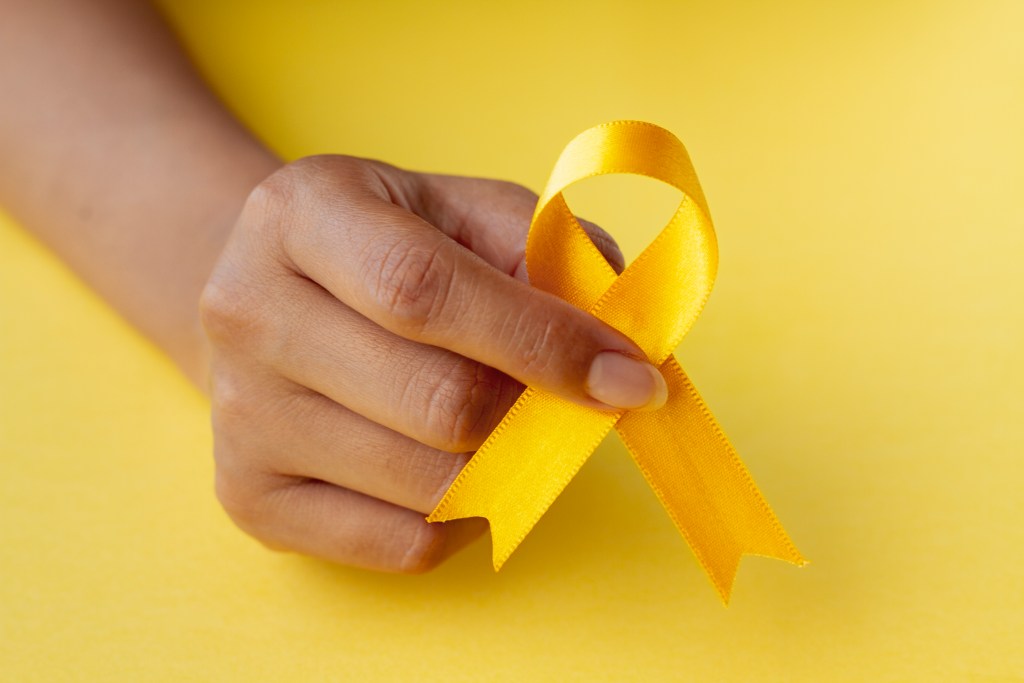 A mão de uma pessoa segura uma fita amarela para ilustrar a campanha e o texto sobre qual a importância do setembro amarelo.